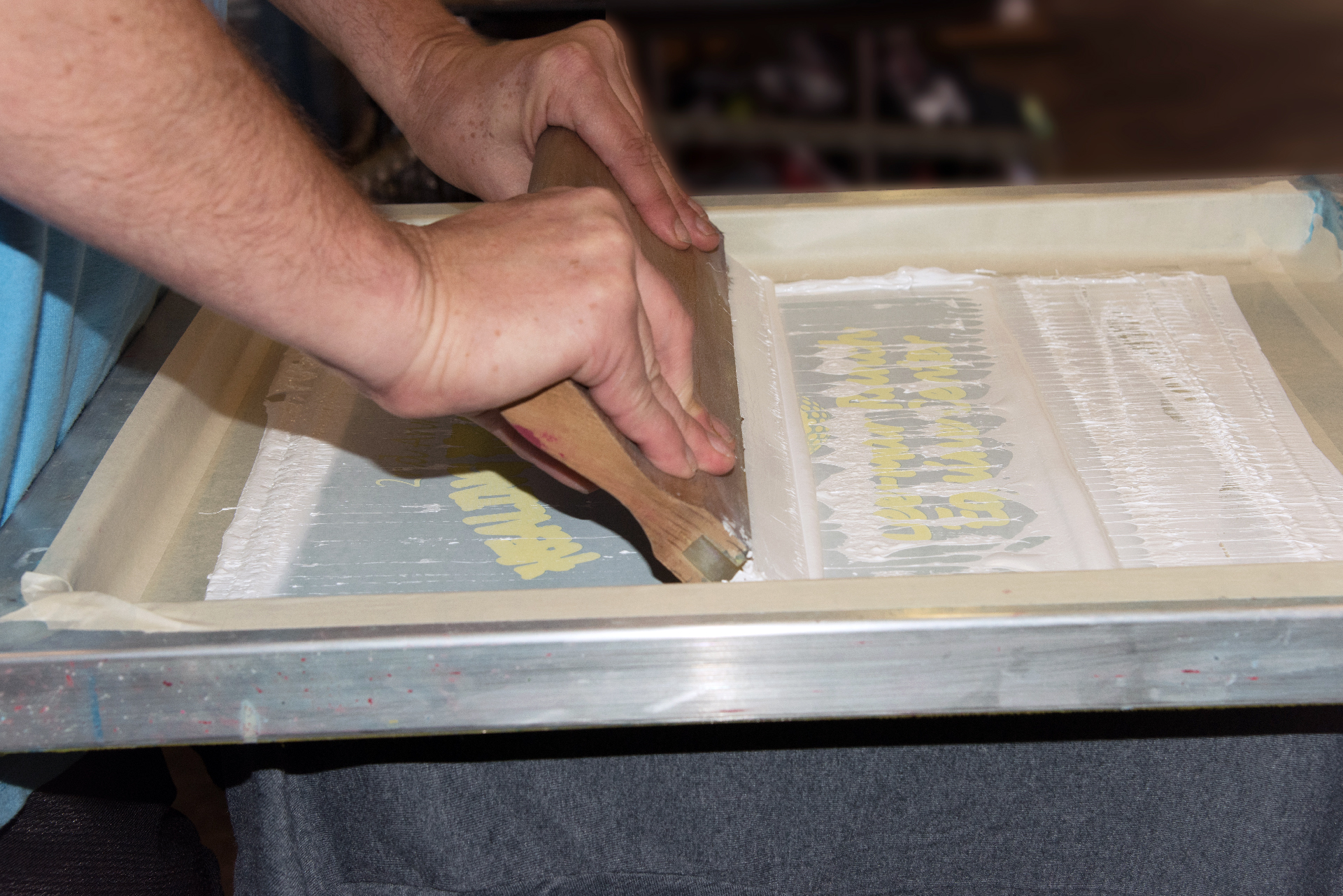 Man dragging ink over screen on a shirt for printing