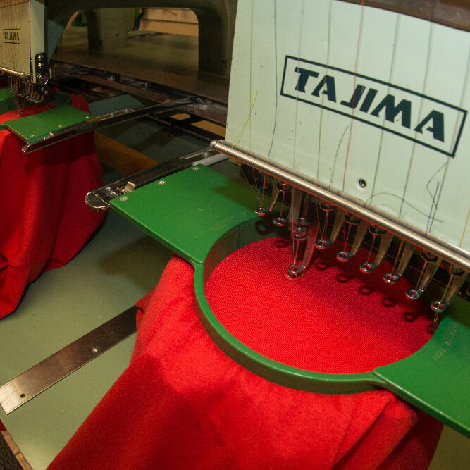 photo of an embroidery machine making a design on a red t-shirt