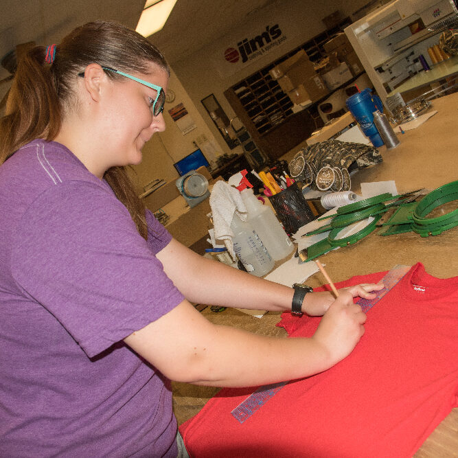 Employee measuring and marking an area on a red t-shirt for embroidery.